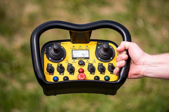 Das Bild zeigt eine ergonomische Fernsteuerung mit Joysticks, Schaltern und einem Not-Aus-Knopf, die zur Steuerung autonomer Geräte wie Mähroboter dient. Das Bild zeigt eine ergonomische Fernsteuerung mit Joysticks, Schaltern und einem Not-Aus-Knopf, die zur Steuerung autonomer Geräte wie Mähroboter dient.